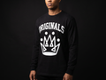 Model wearing Originals matte-black long sleeve tee with white ORIGINALS crown across chest