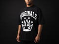 Model wearing Originals matte-black oversized logo tee with large white ORIGINALS crown across chest